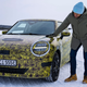 A photo of Mini head of design Oliver Heilmer patting the front of a camouflage test car.